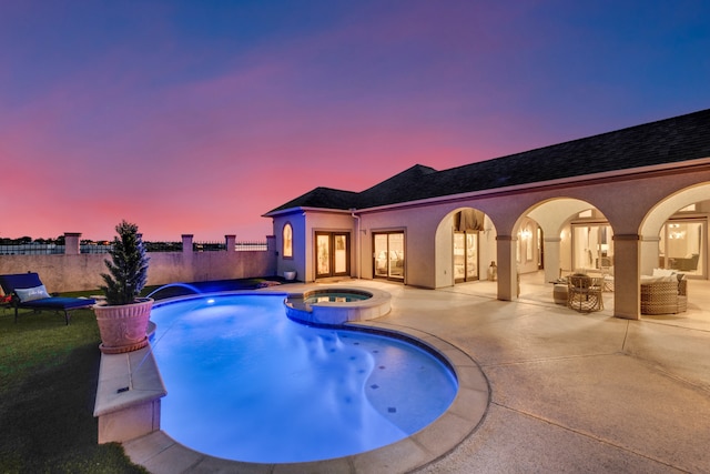 pool at dusk featuring a patio area, pool water feature, and an in ground hot tub