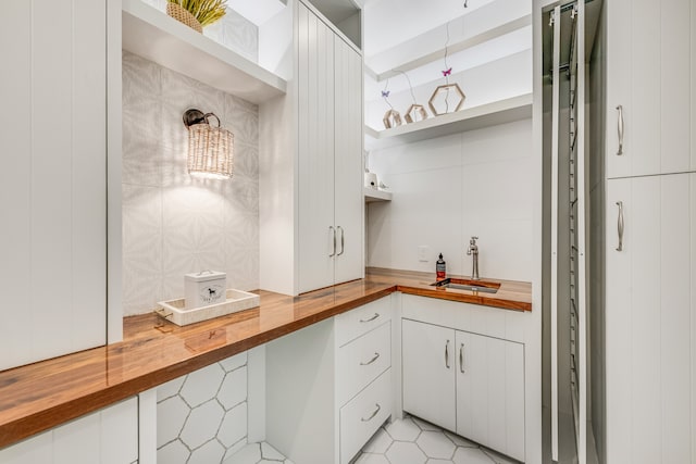 kitchen with butcher block countertops, sink, light tile floors, and white cabinetry