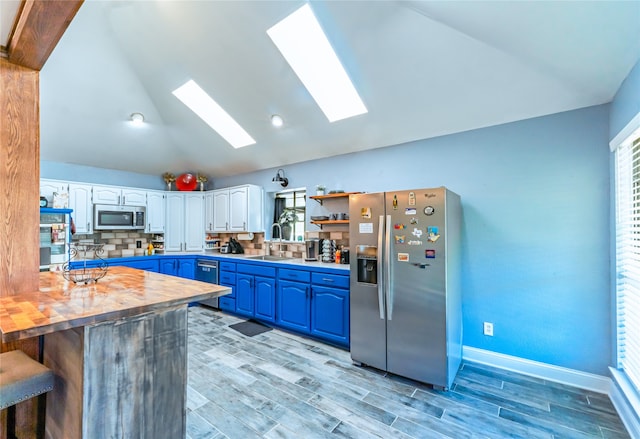 kitchen featuring lofted ceiling with skylight, white cabinetry, blue cabinetry, stainless steel appliances, and kitchen peninsula