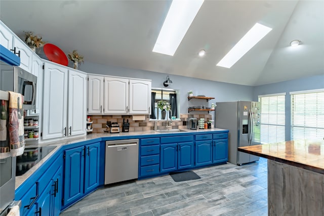 kitchen featuring appliances with stainless steel finishes, backsplash, lofted ceiling with skylight, white cabinets, and blue cabinets