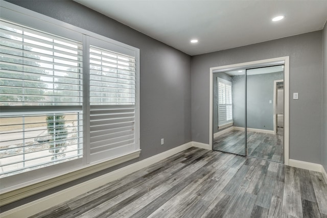 unfurnished bedroom with wood-type flooring, a closet, and multiple windows