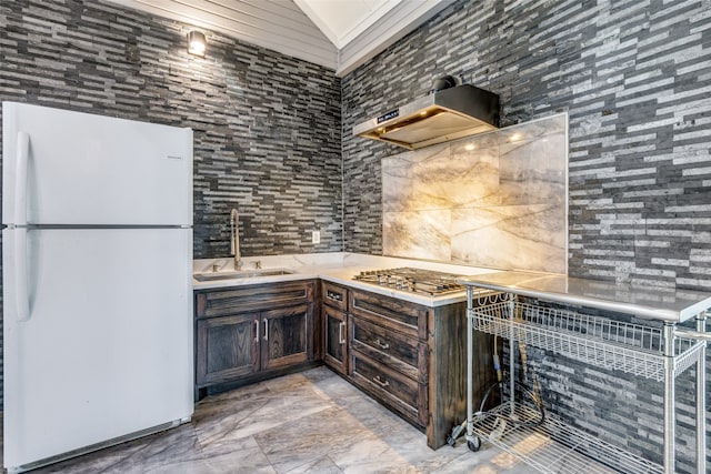 kitchen featuring white refrigerator, dark brown cabinetry, light tile floors, wall chimney exhaust hood, and sink