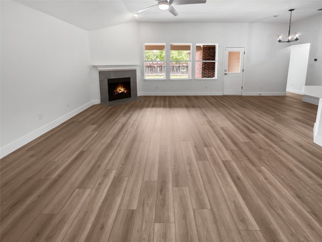 unfurnished living room featuring a fireplace, ceiling fan with notable chandelier, hardwood / wood-style floors, and lofted ceiling