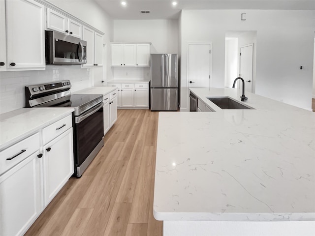 kitchen with white cabinetry, light hardwood / wood-style flooring, stainless steel appliances, light stone counters, and sink