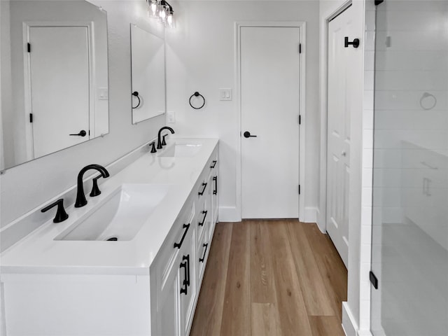 bathroom featuring a tile shower, dual bowl vanity, and wood-type flooring