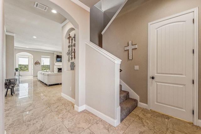 stairs featuring a stone fireplace, light tile floors, and crown molding