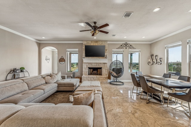 tiled living room featuring a stone fireplace, ceiling fan, a textured ceiling, and ornamental molding