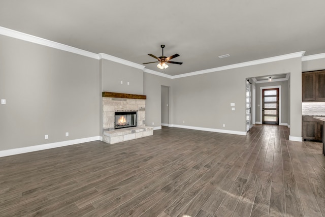 unfurnished living room with ornamental molding, dark wood-type flooring, ceiling fan, and a stone fireplace