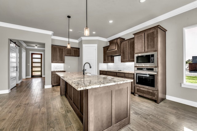 kitchen featuring tasteful backsplash, light stone counters, stainless steel appliances, hardwood / wood-style flooring, and an island with sink