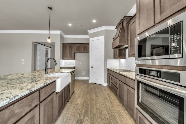 kitchen with light hardwood / wood-style floors, sink, light stone counters, appliances with stainless steel finishes, and a barn door