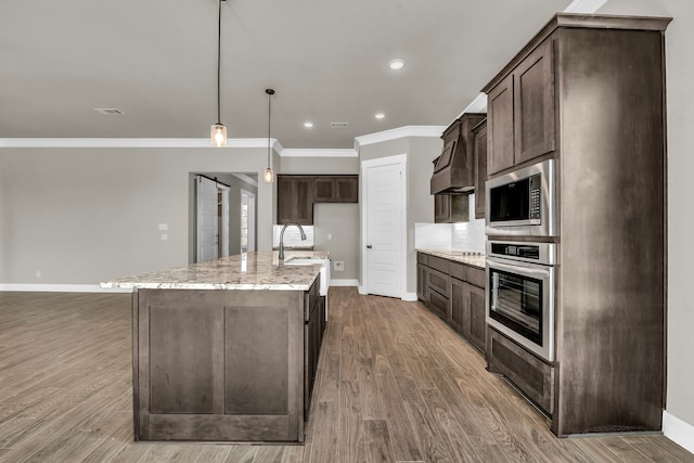 kitchen featuring hardwood / wood-style floors, stainless steel appliances, hanging light fixtures, and an island with sink