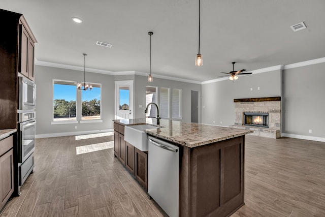 kitchen with stainless steel appliances, sink, a fireplace, hanging light fixtures, and light hardwood / wood-style flooring