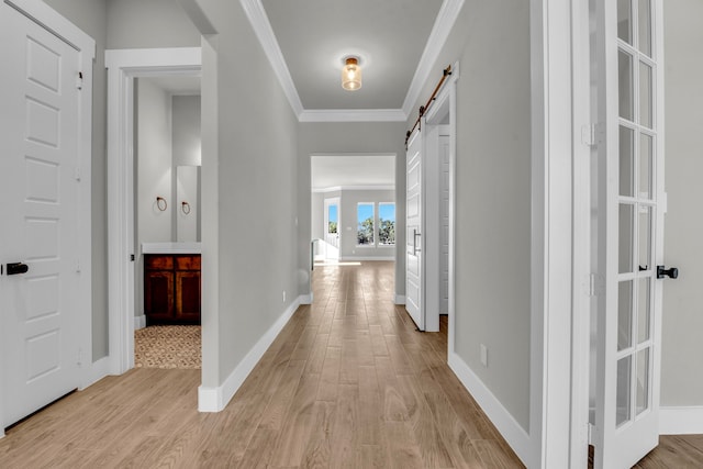 hallway with light wood-type flooring, a barn door, and crown molding