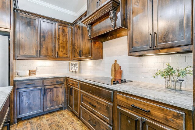 kitchen with light stone counters, ornamental molding, dark brown cabinets, light hardwood / wood-style flooring, and black electric stovetop