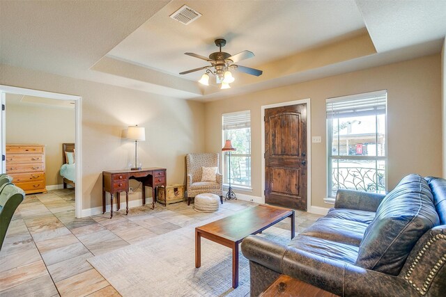 living room with ceiling fan, a raised ceiling, and a wealth of natural light