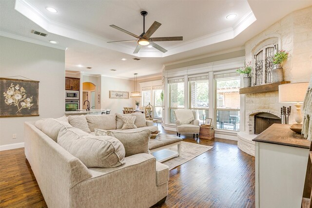 living room featuring ceiling fan, a raised ceiling, dark wood-type flooring, and a stone fireplace