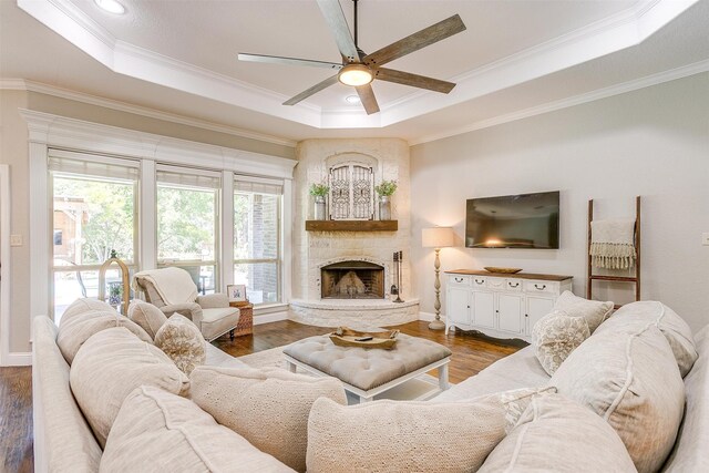 living room featuring wood-type flooring, a raised ceiling, a fireplace, and ceiling fan