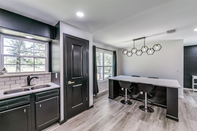 kitchen featuring decorative light fixtures, light wood finished floors, light countertops, decorative backsplash, and a sink