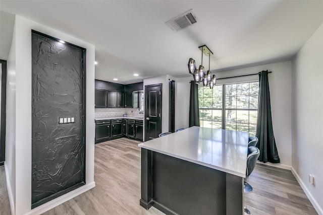 kitchen featuring light wood-style flooring, visible vents, light countertops, decorative backsplash, and decorative light fixtures