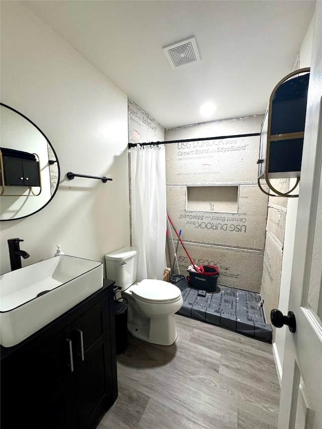 bathroom featuring toilet, wood finished floors, vanity, visible vents, and a stall shower