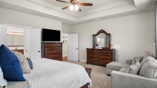 carpeted bedroom with a tray ceiling, ensuite bath, and ceiling fan