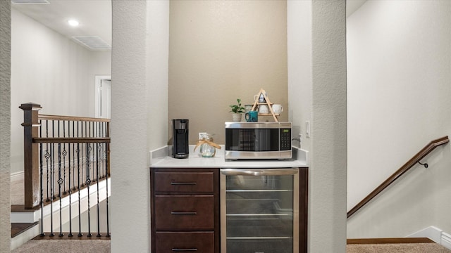 bar featuring dark brown cabinets, light carpet, and wine cooler