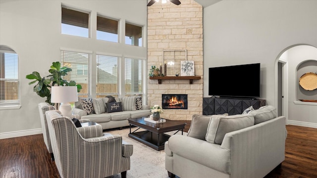 living room featuring dark hardwood / wood-style floors, ceiling fan, a fireplace, and a high ceiling