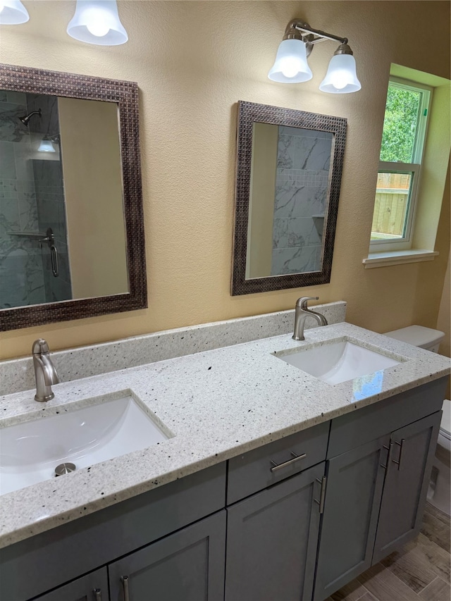 bathroom featuring double sink vanity, tiled shower, and toilet