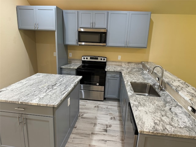 kitchen with light stone counters, light hardwood / wood-style flooring, a center island, appliances with stainless steel finishes, and sink