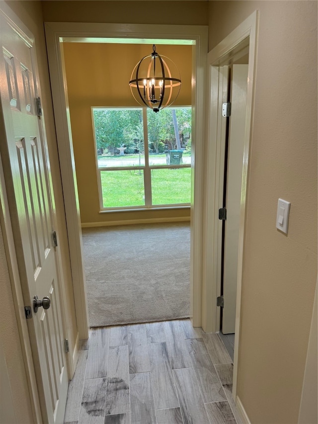 corridor with light carpet and an inviting chandelier