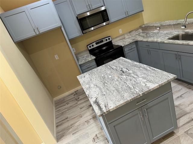 kitchen featuring light hardwood / wood-style floors, light stone countertops, gray cabinetry, stainless steel appliances, and sink