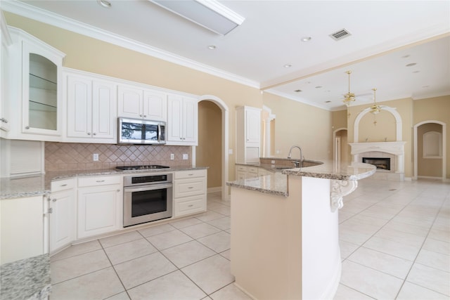 kitchen featuring tasteful backsplash, white cabinets, appliances with stainless steel finishes, light stone counters, and light tile patterned floors