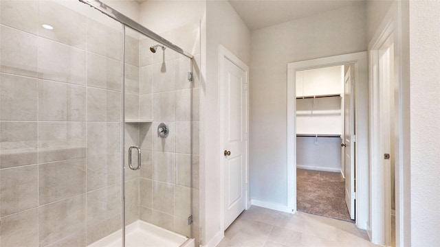 bathroom featuring a stall shower, tile patterned flooring, a spacious closet, and baseboards