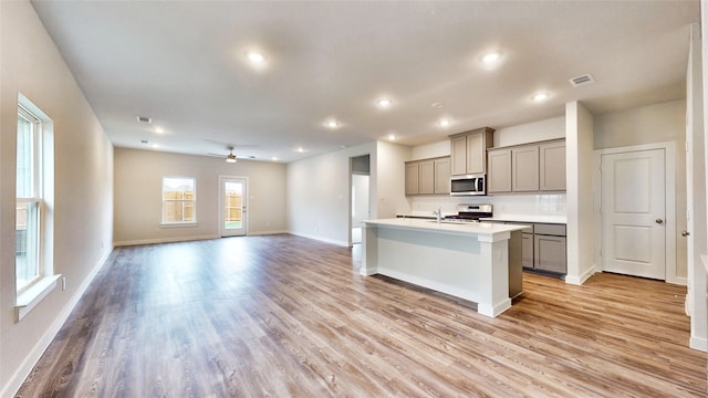 kitchen featuring light wood-type flooring, gray cabinetry, stainless steel appliances, ceiling fan, and an island with sink