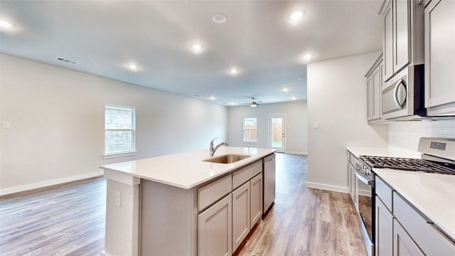 kitchen featuring an island with sink, stainless steel appliances, gray cabinetry, and sink