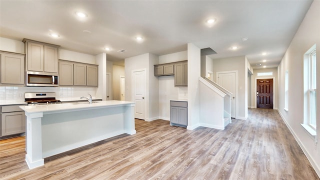 kitchen featuring gray cabinetry, a kitchen island with sink, light hardwood / wood-style flooring, tasteful backsplash, and stainless steel appliances