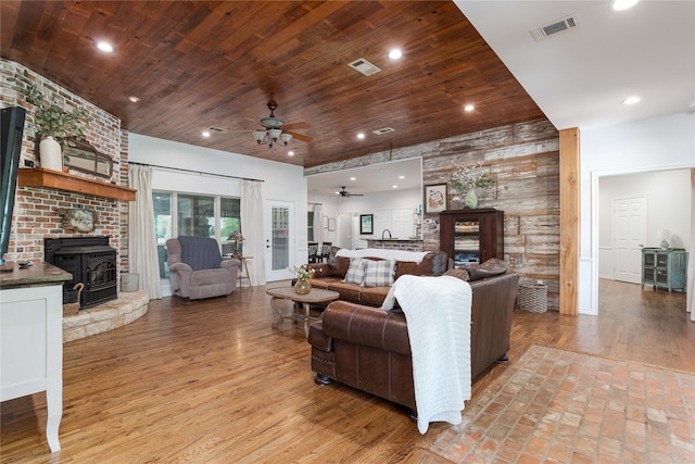 living room with a large fireplace, a wood stove, ceiling fan, wooden ceiling, and wood-type flooring