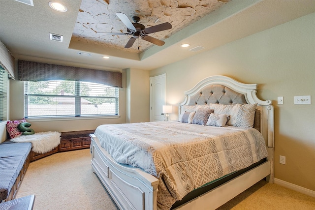 bedroom with light carpet, ceiling fan, a tray ceiling, and a textured ceiling