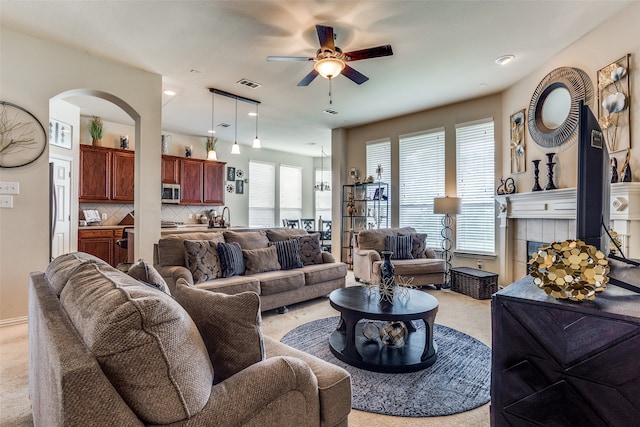 living room featuring ceiling fan, a fireplace, sink, and light carpet