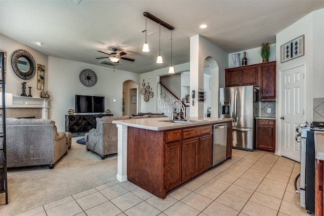 kitchen featuring appliances with stainless steel finishes, light colored carpet, ceiling fan, sink, and a center island with sink