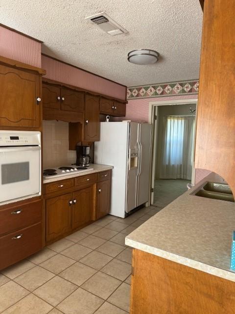 kitchen featuring sink, white appliances, light tile patterned floors, and a textured ceiling