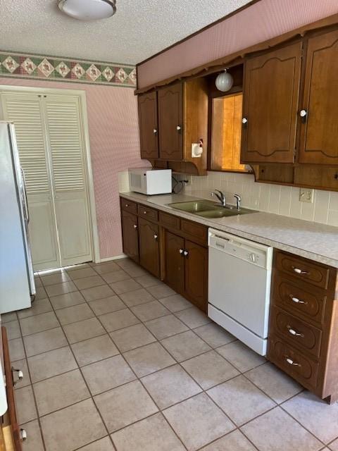 kitchen featuring sink, white appliances, a textured ceiling, and light tile patterned flooring