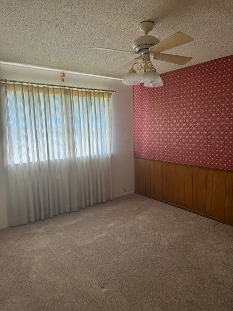 spare room featuring a textured ceiling, wooden walls, carpet, and ceiling fan