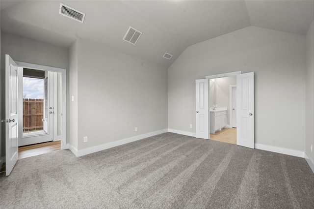 unfurnished bedroom with light colored carpet, lofted ceiling, and ensuite bathroom