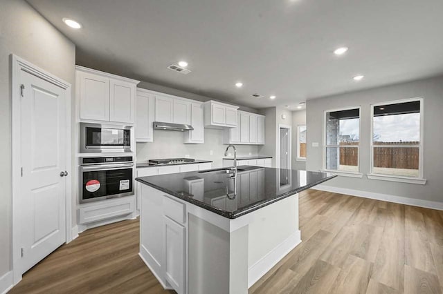 kitchen with white cabinetry, sink, stainless steel appliances, and an island with sink