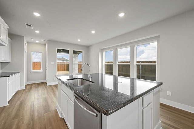 kitchen featuring white cabinetry, sink, dark stone countertops, stainless steel dishwasher, and a center island with sink