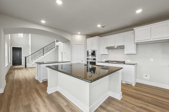 kitchen with an island with sink, sink, stainless steel microwave, and white cabinets