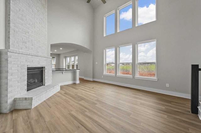 unfurnished living room featuring a brick fireplace, a towering ceiling, light hardwood / wood-style flooring, and ceiling fan