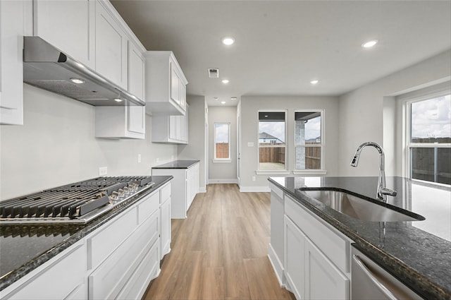 kitchen with appliances with stainless steel finishes, white cabinetry, sink, dark stone countertops, and wall chimney exhaust hood