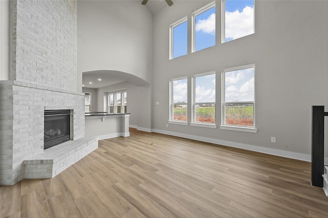 unfurnished living room with a brick fireplace, light hardwood / wood-style flooring, ceiling fan, and a high ceiling